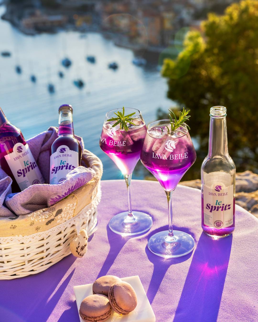 Picknick mit Lav'a Belle le Spritz: Flaschen im Korb, zwei Gläser mit Rosmarin und Macarons über einer Bucht